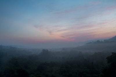 Wide landscape of misty hills at dawn, with soft earth tones blending into the sky.