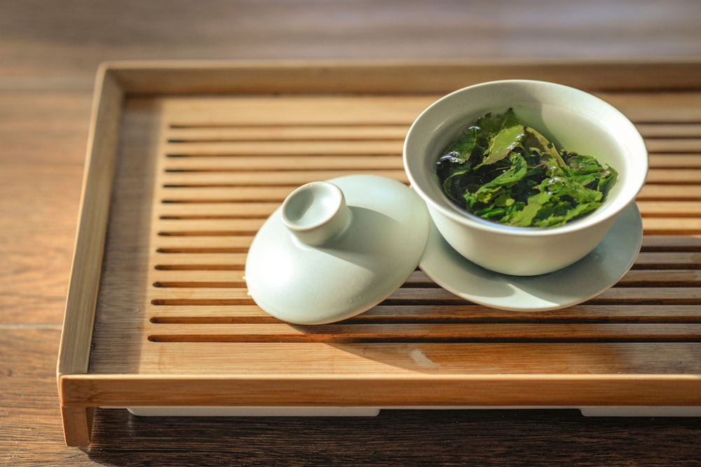 Hojas de té verde en cuenco de cerámica blanca con tapa abierta