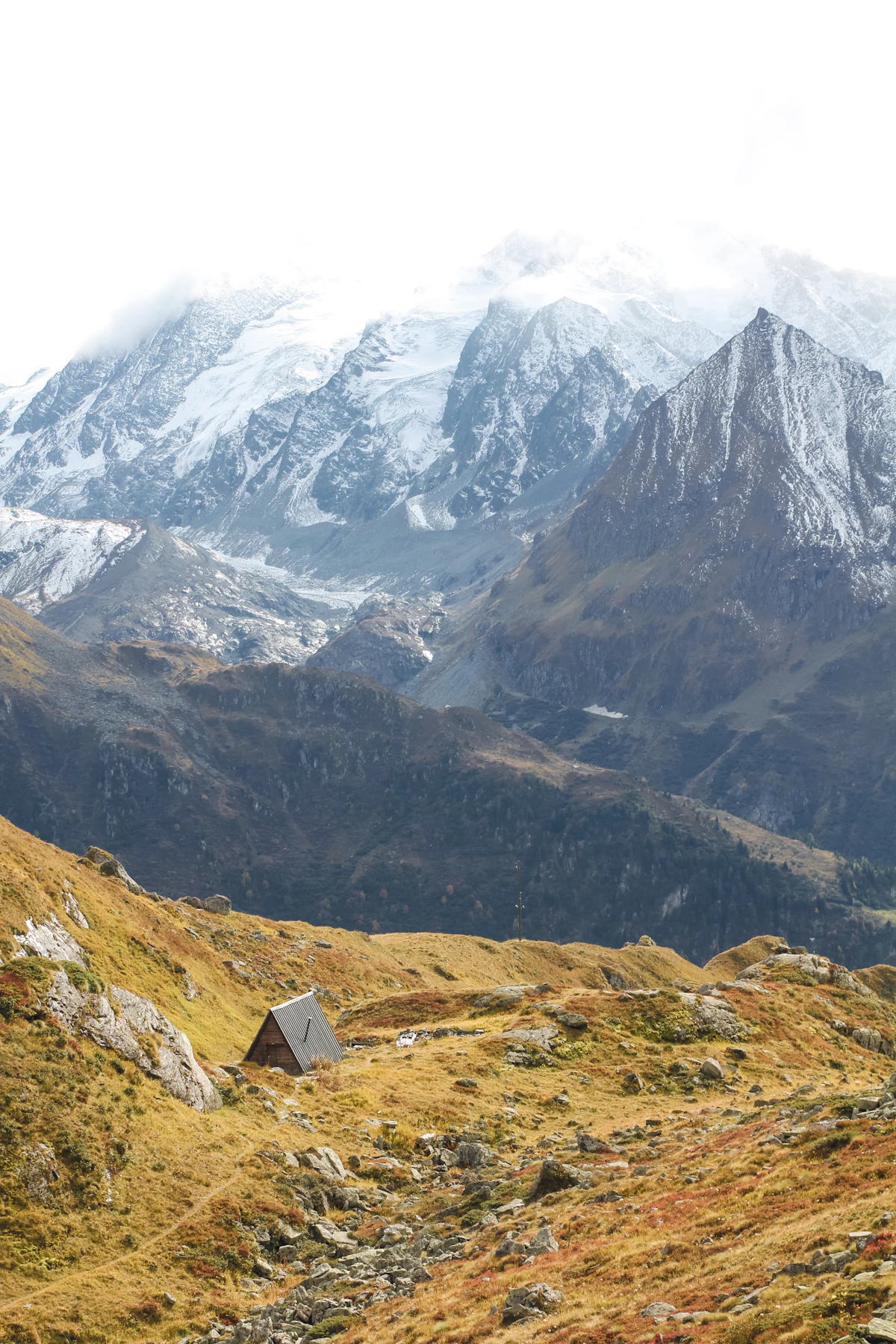 A small hut on an autumn hillside near Verbier, below glaciated peaks in cloud