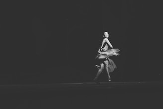 A ballet dancer is captured mid-performance with a graceful expression and flowing dress, moving elegantly on a dimly lit stage.