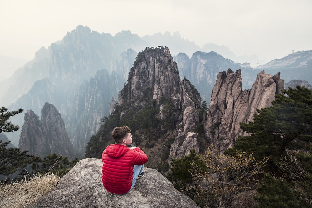 man sitting by cliff facing mountain