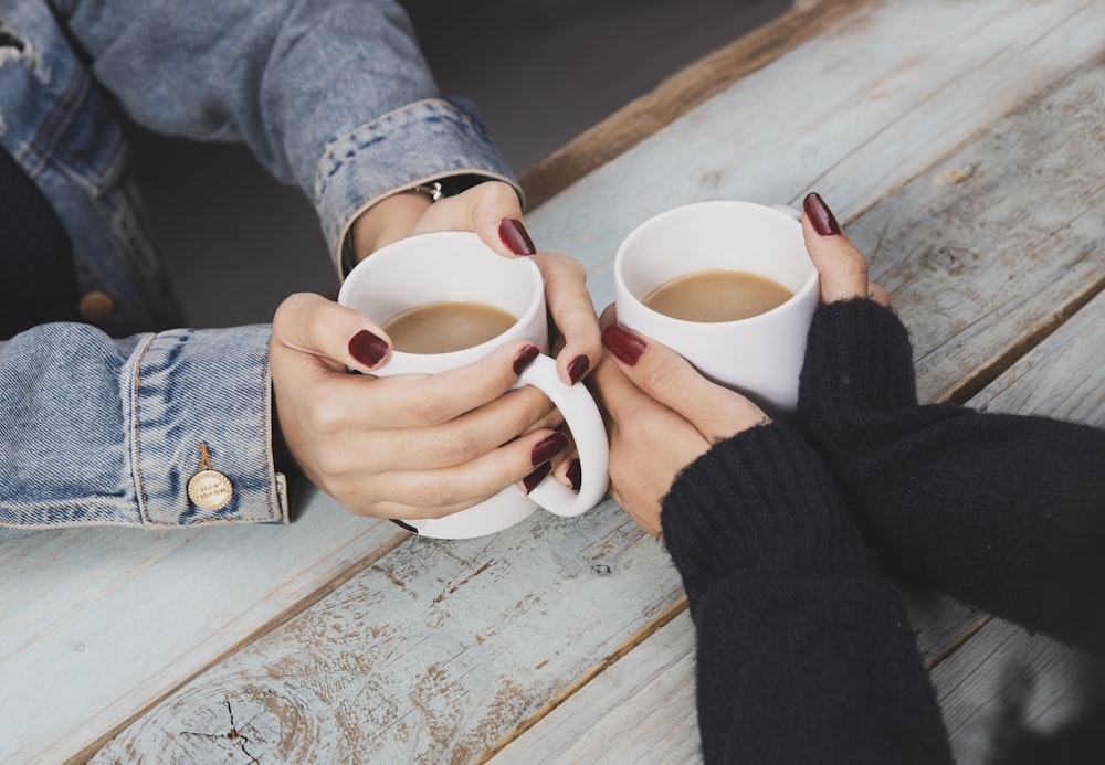 two persons holding white ceramic mugs