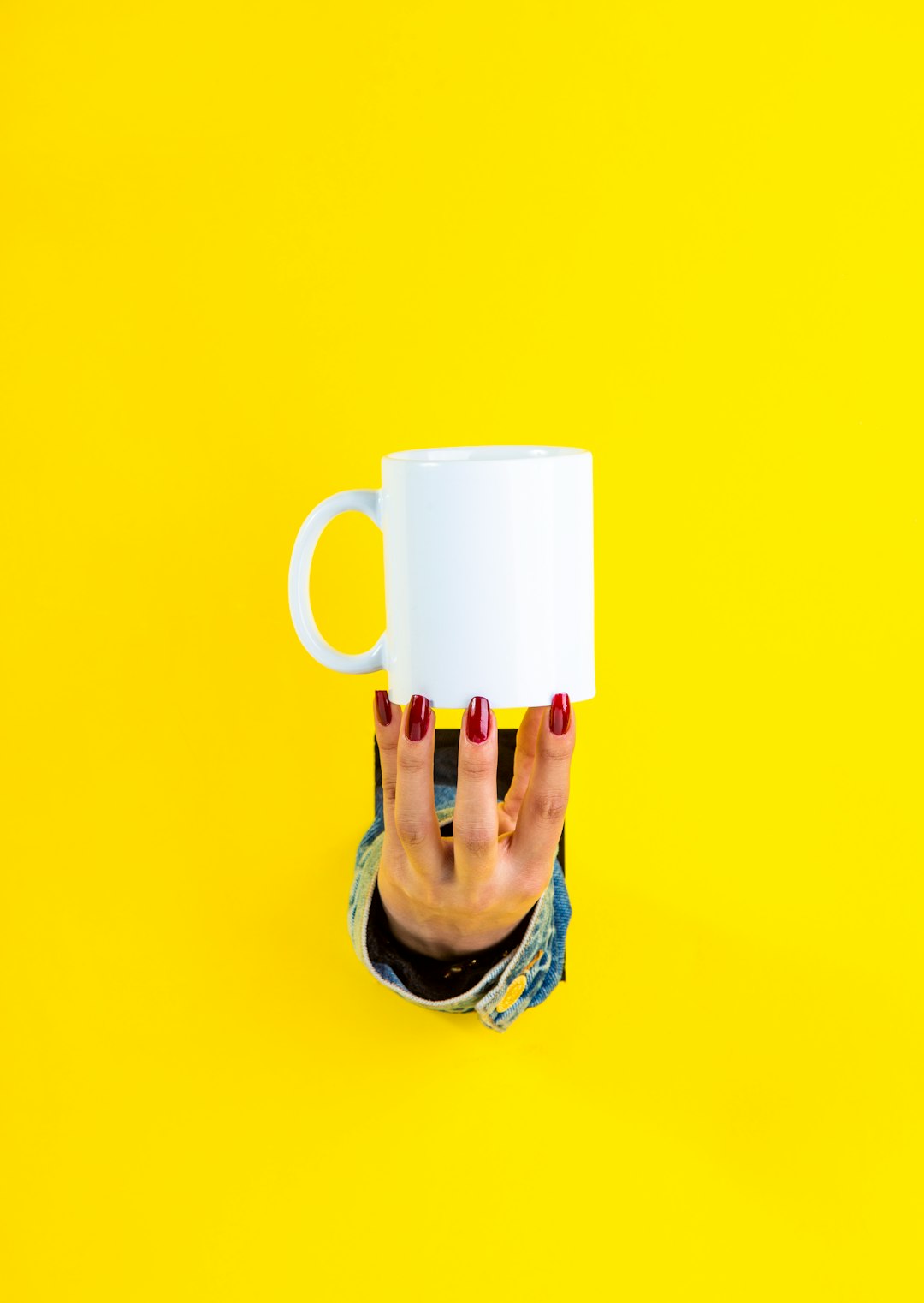 red nail polished hand holding white ceramic mug by fingertips