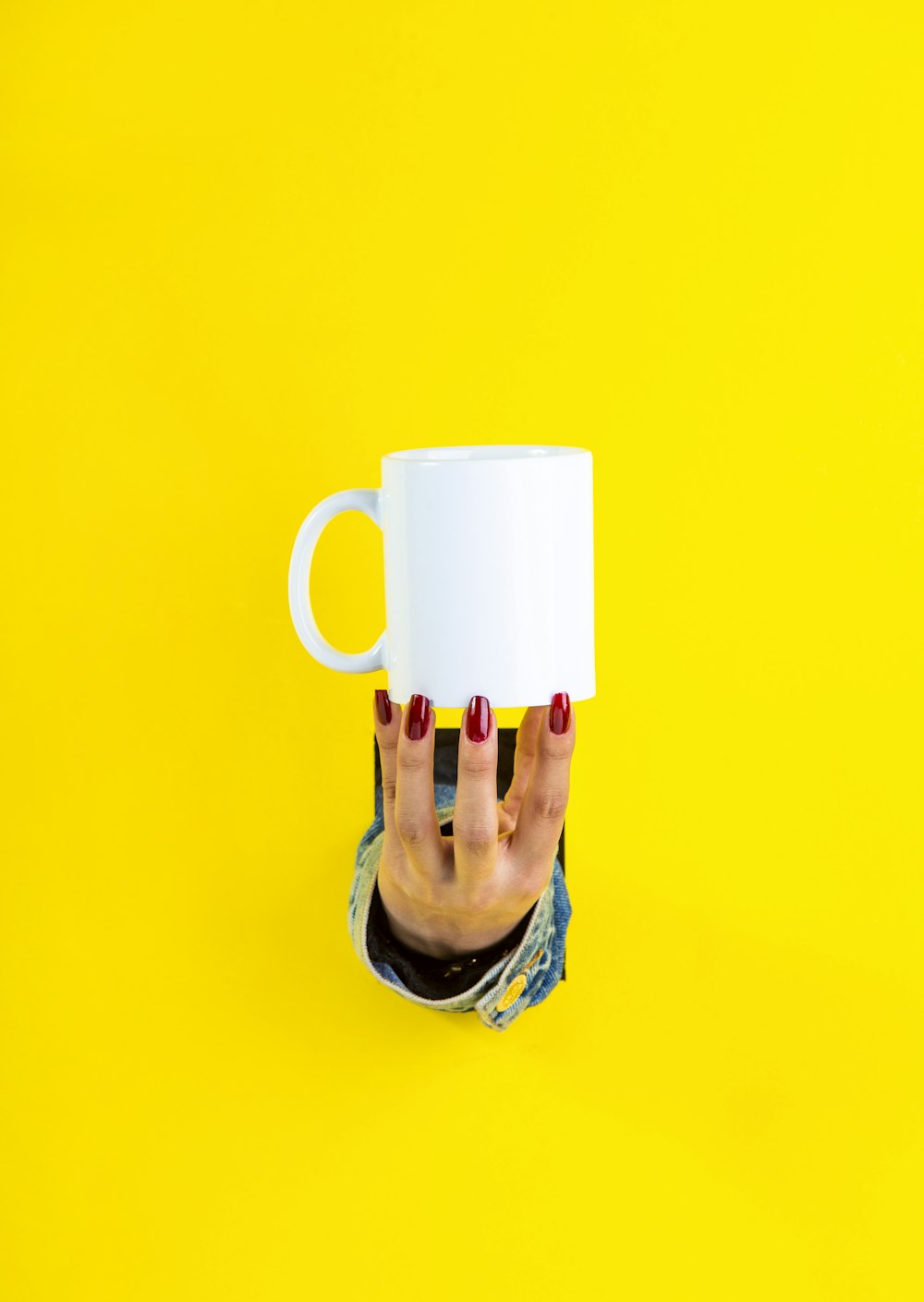 red nail polished hand holding white ceramic mug by fingertips