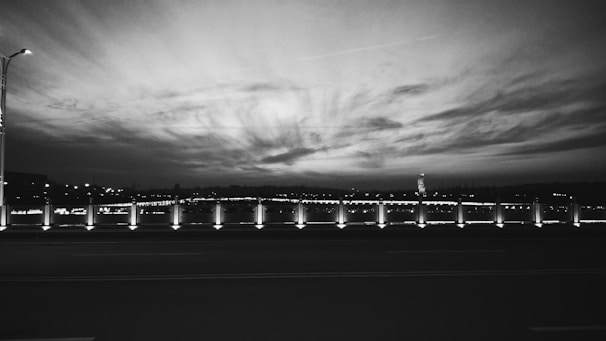 A black and white photograph capturing a serene urban landscape at dusk.