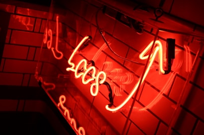 Neon lights in vibrant red color with cursive lettering mounted against a tiled wall, creating a warm and intense glow.