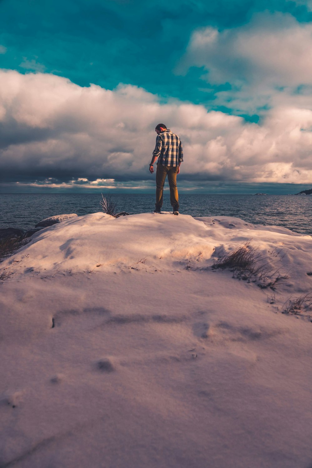 man standing on snow covered land while facing body of water