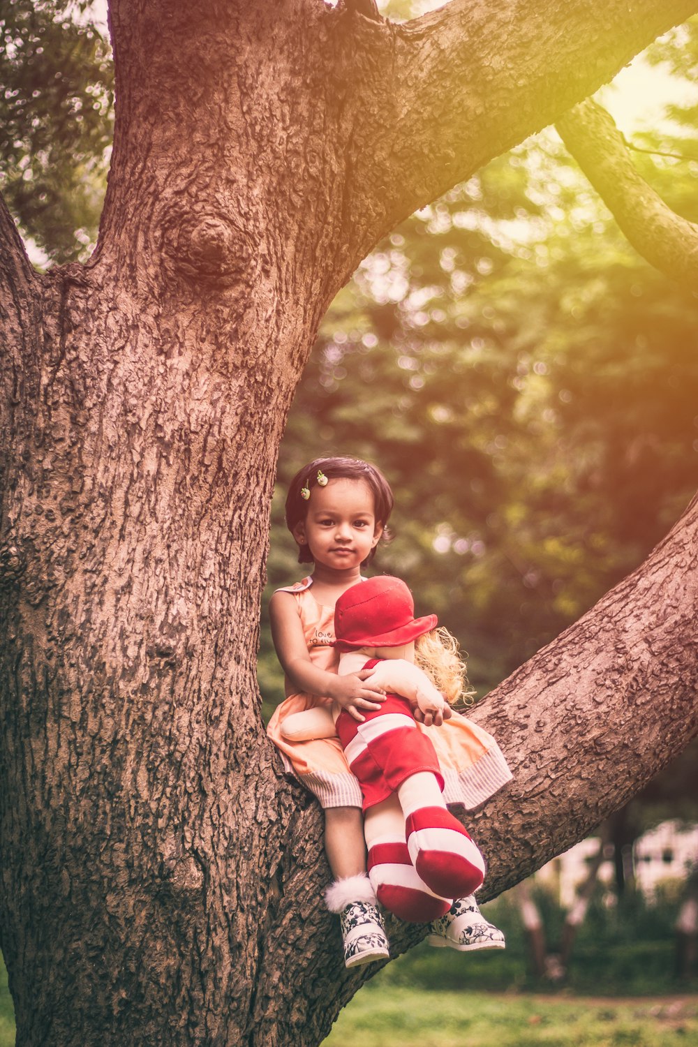 girl sitting on tree branch holding doll