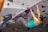 A woman is engaged in indoor rock climbing, gripping holds on a climbing wall with vibrant colors. She wears a turquoise tank top and patterned climbing pants. The climbing wall is filled with various holds and routes marked by different colors and numbers.