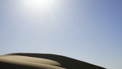 Wind-swept dunes with a Kalima surf bag resting on the sand under a clear blue sky.