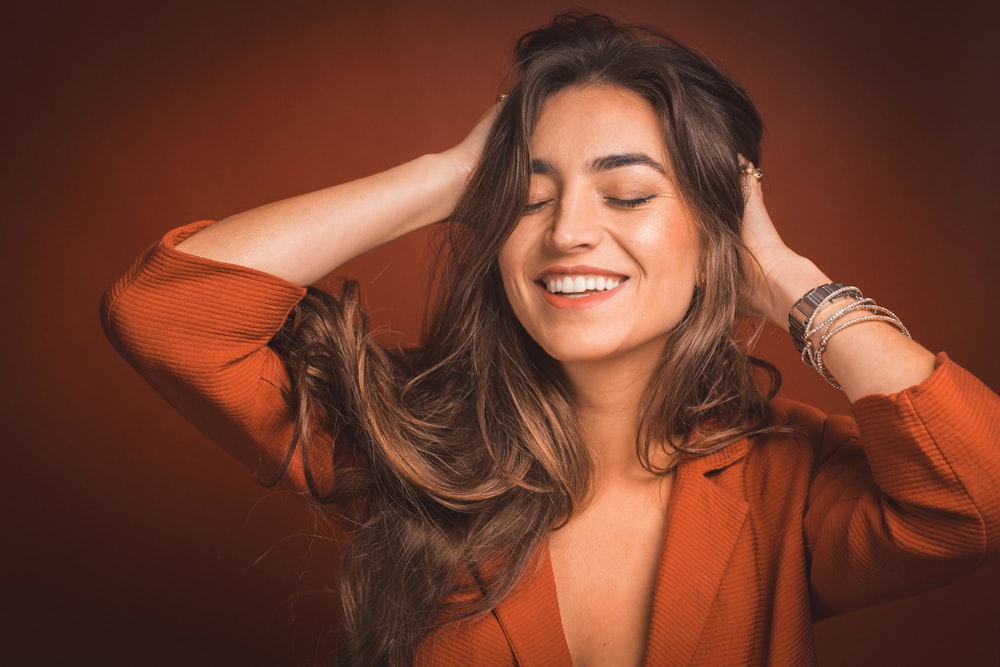 smiling woman in brown top holding hairs