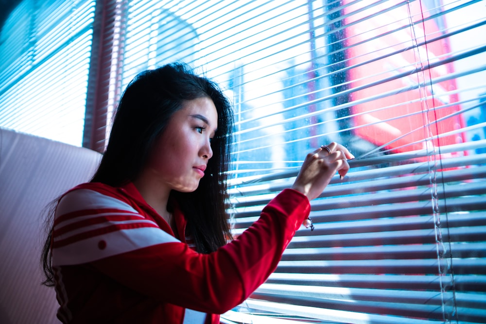 woman holding on window blinds during daytime