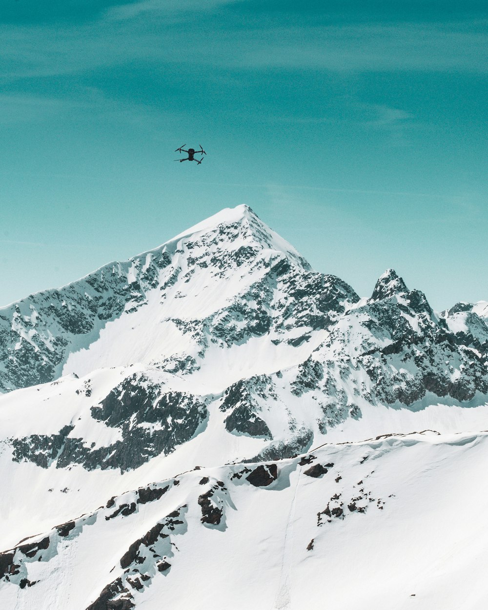 雪に覆われた山の下の空中に浮かぶ黒いクワッドコプタードローン