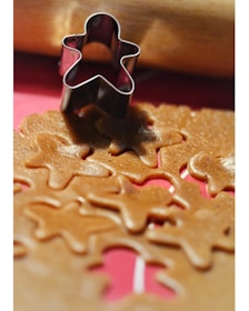 A metal gingerbread man-shaped cookie cutter is placed on a sheet of rolled-out dough that has several cutouts of the same shape. A wooden rolling pin can be seen in the background.