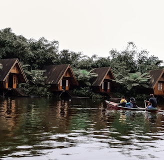 three men riding kayak on body of water leading to wooden cottages