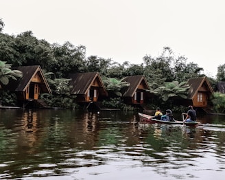 three men riding kayak on body of water leading to wooden cottages