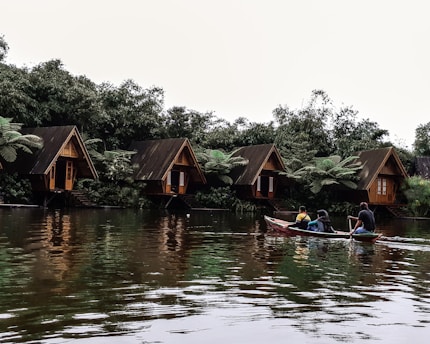 three men riding kayak on body of water leading to wooden cottages