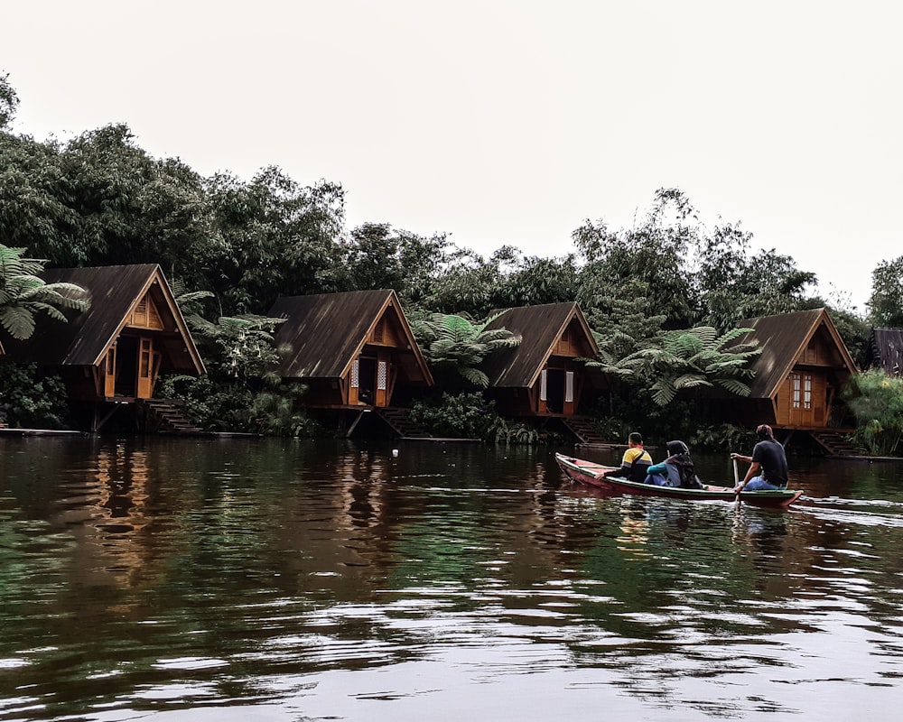 three men riding kayak on body of water leading to wooden cottages