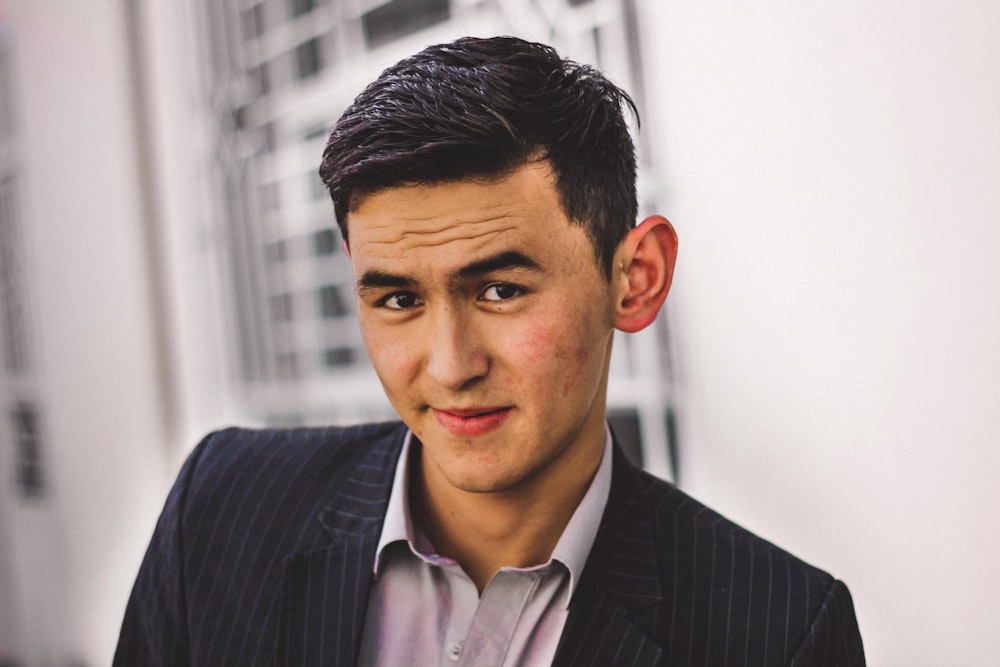 man in black blazer smiling by wall