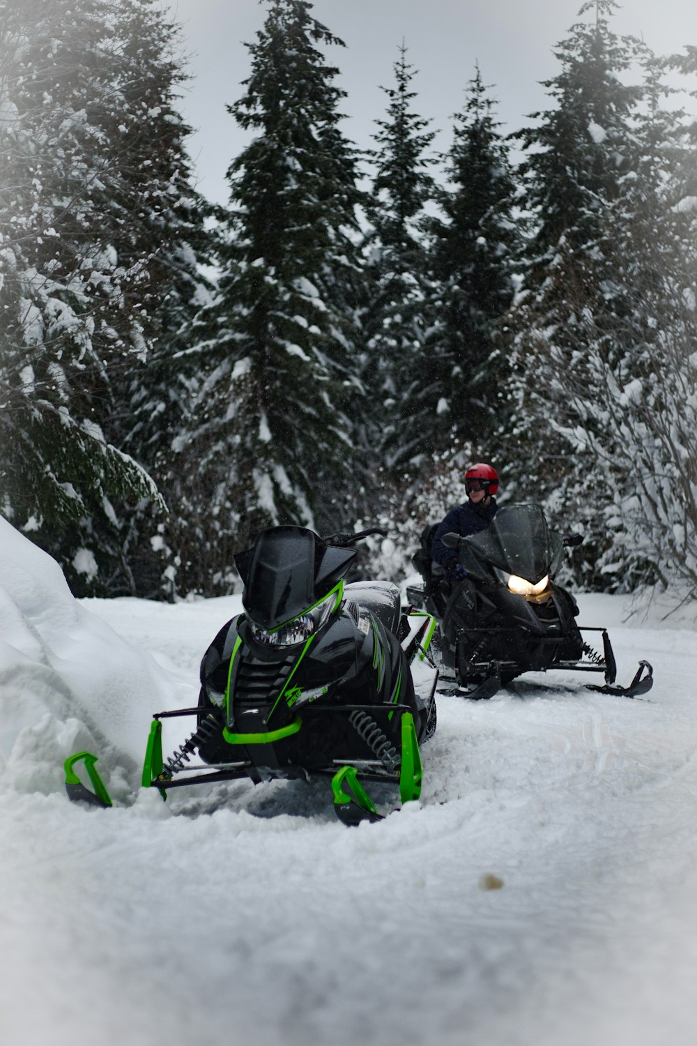 Moto de nieve verde y negra junto a moto de nieve negra durante el día