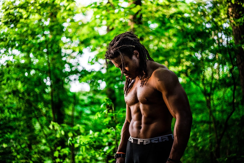 topless man looking down near green trees during daytime