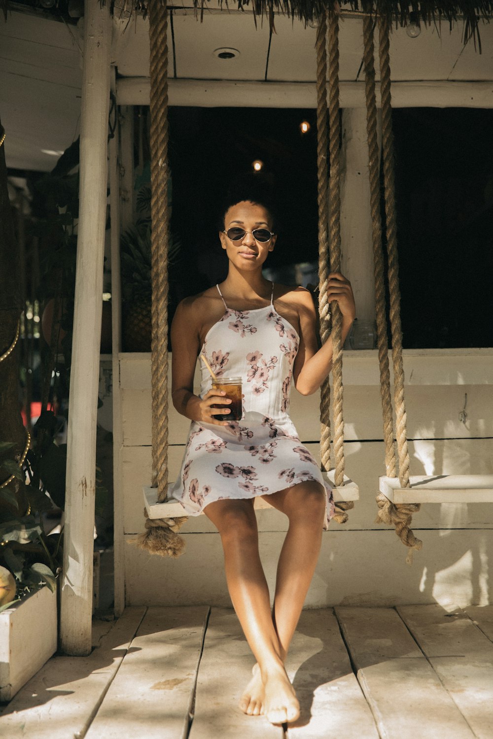 woman wearing dress sitting on swing holding drinking glass