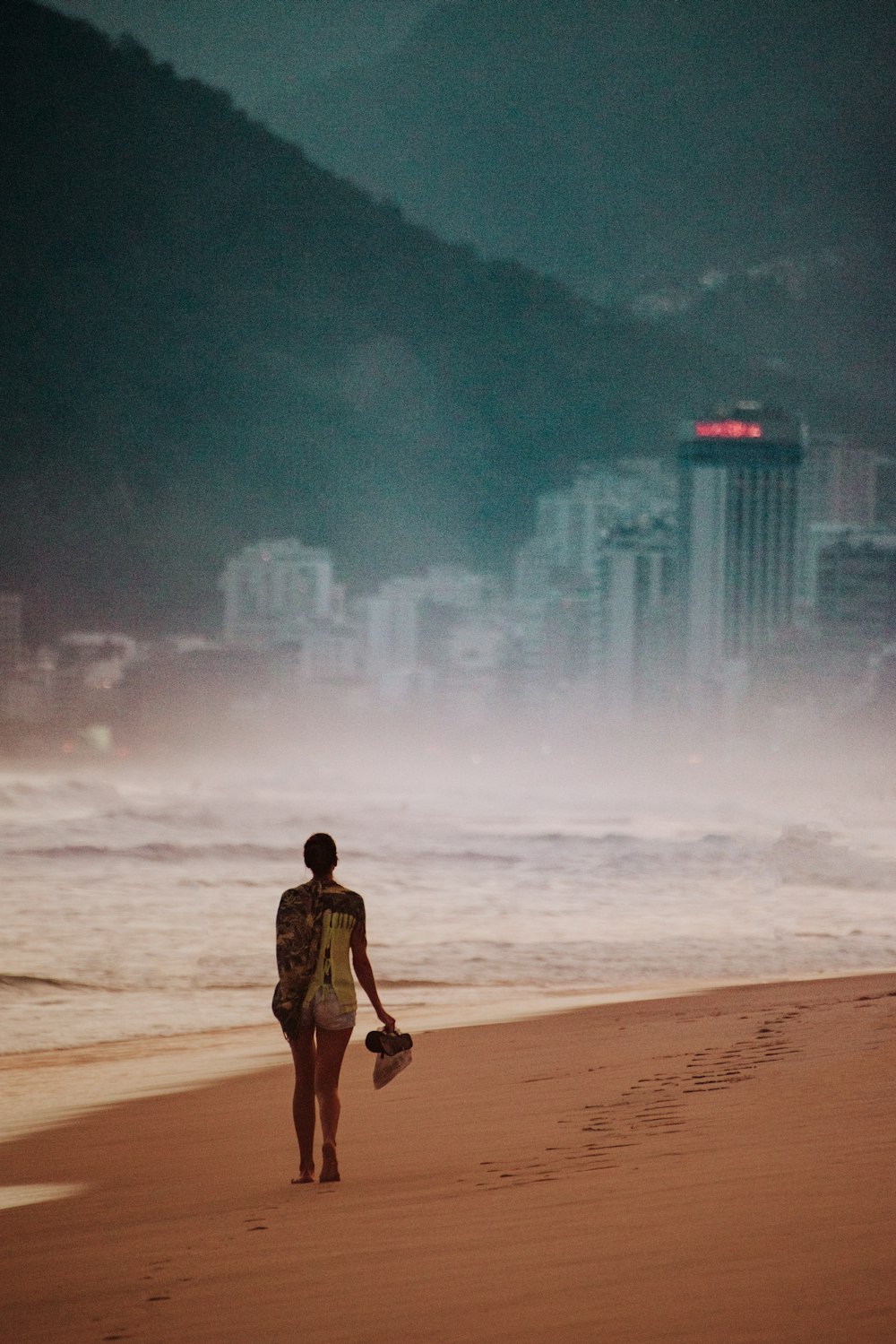 muchacha que camina en la orilla del mar a través del edificio de la ciudad