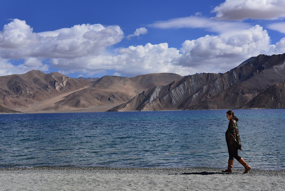 woman wearing jacket walking on seashore during daytime