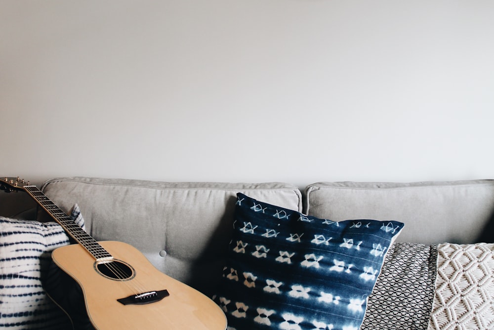 brown acoustic guitar near throw pillow on sofa