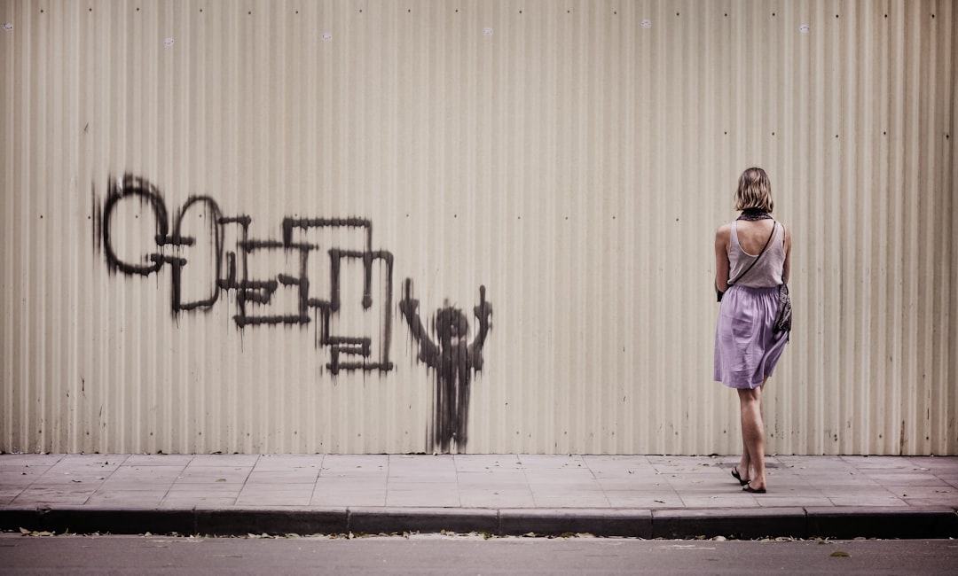 woman in white tank top and purple skirt stands facing graffiti painted wall