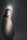 A person is standing in a spotlight with a dark background, wearing a light-colored suit. The lighting creates a dramatic shadow on the wall, and the person looks contemplative.