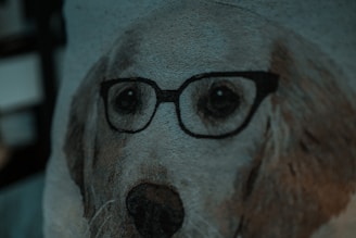 A close-up view of a woven fabric depicting a dog's face wearing glasses. The texture of the fabric is visible, with various shades of beige and brown highlighting the dog's features against a muted background.