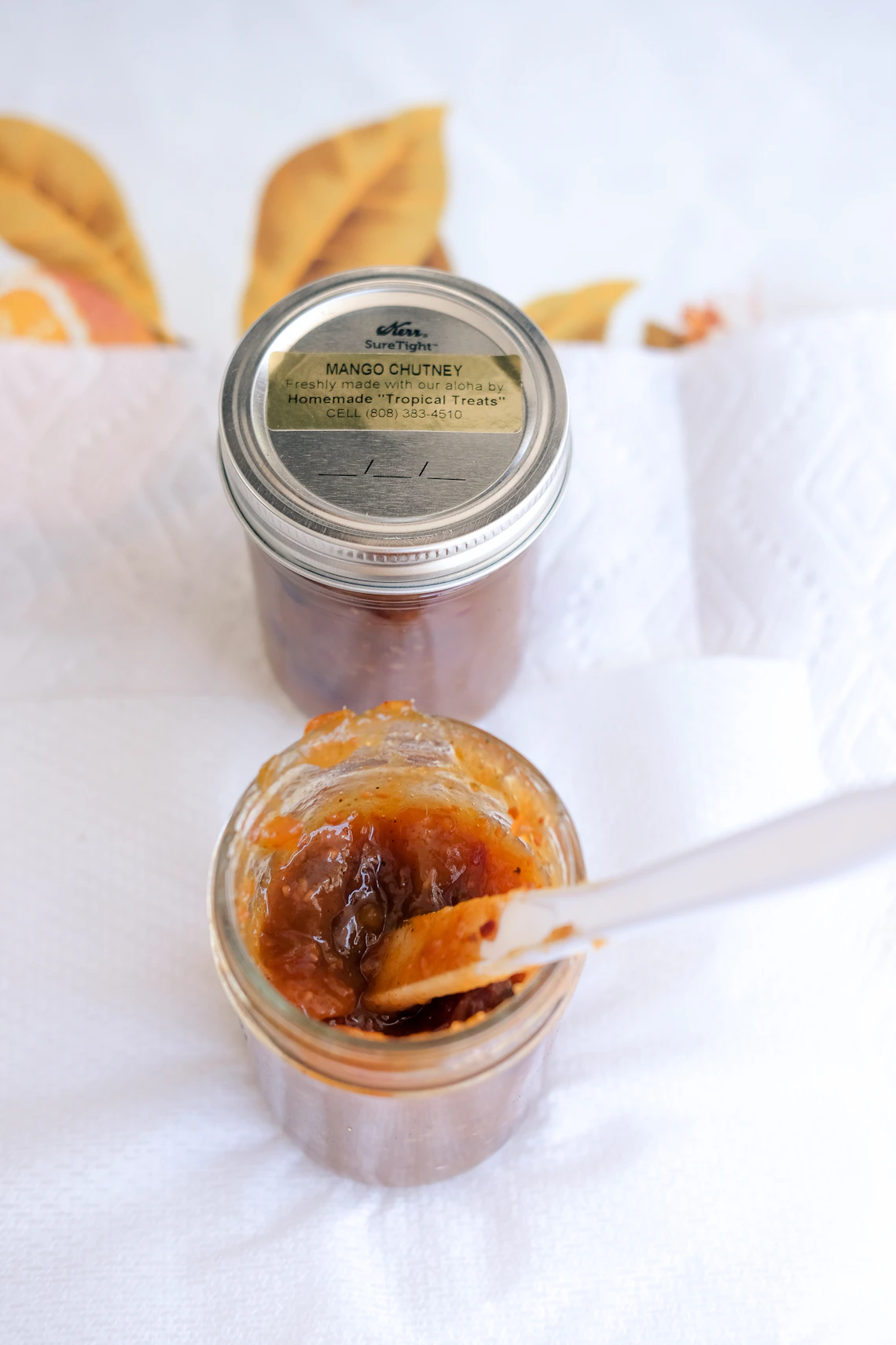 A glass jar of fruit preserves accompanied by a serving spoon.