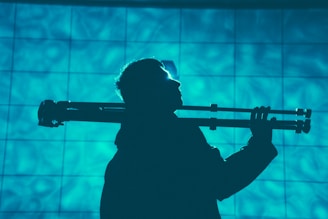 A silhouette of a person holding a tripod over their shoulder, set against a textured blue background with a tiled grid pattern.