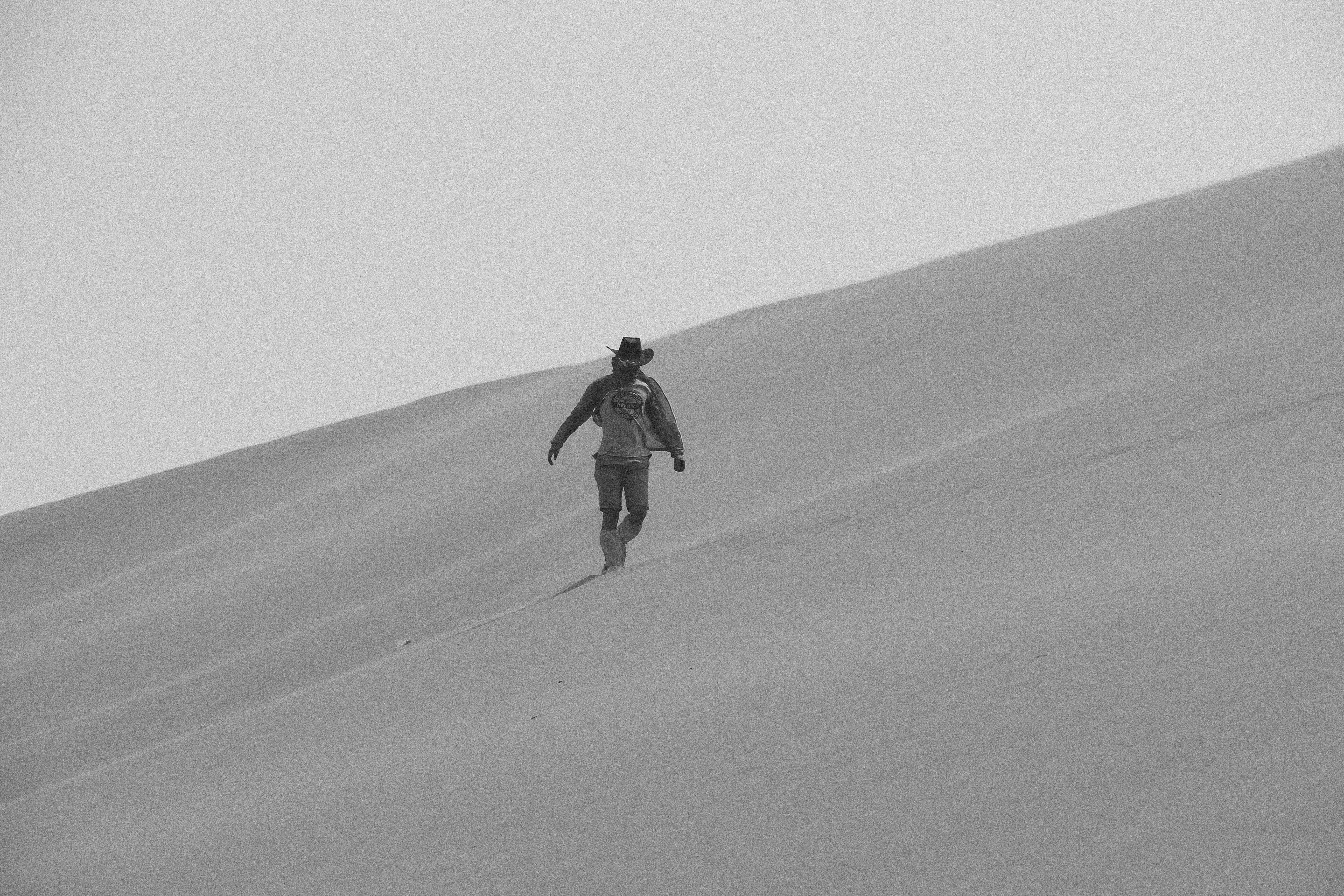 person wearing hat walking on desert during daytime