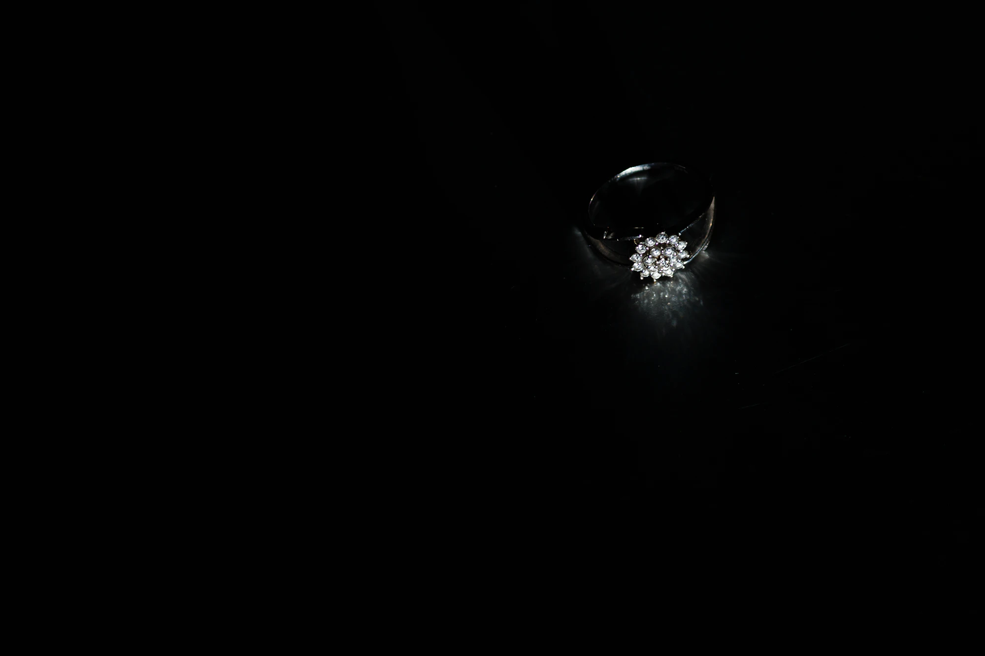 A diamond cluster ring catching a single beam of light in darkness