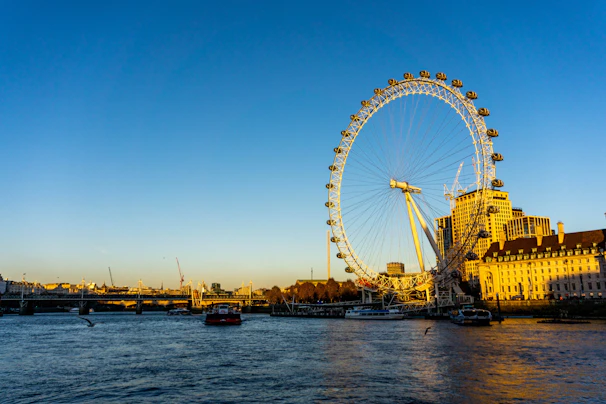 The iconic London Eye towering over the Thames, captured on a clear sunny day with families enjoying around.