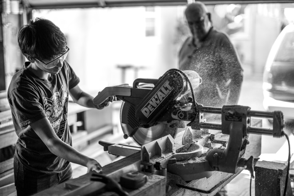 grayscale photography of boy using miter saw