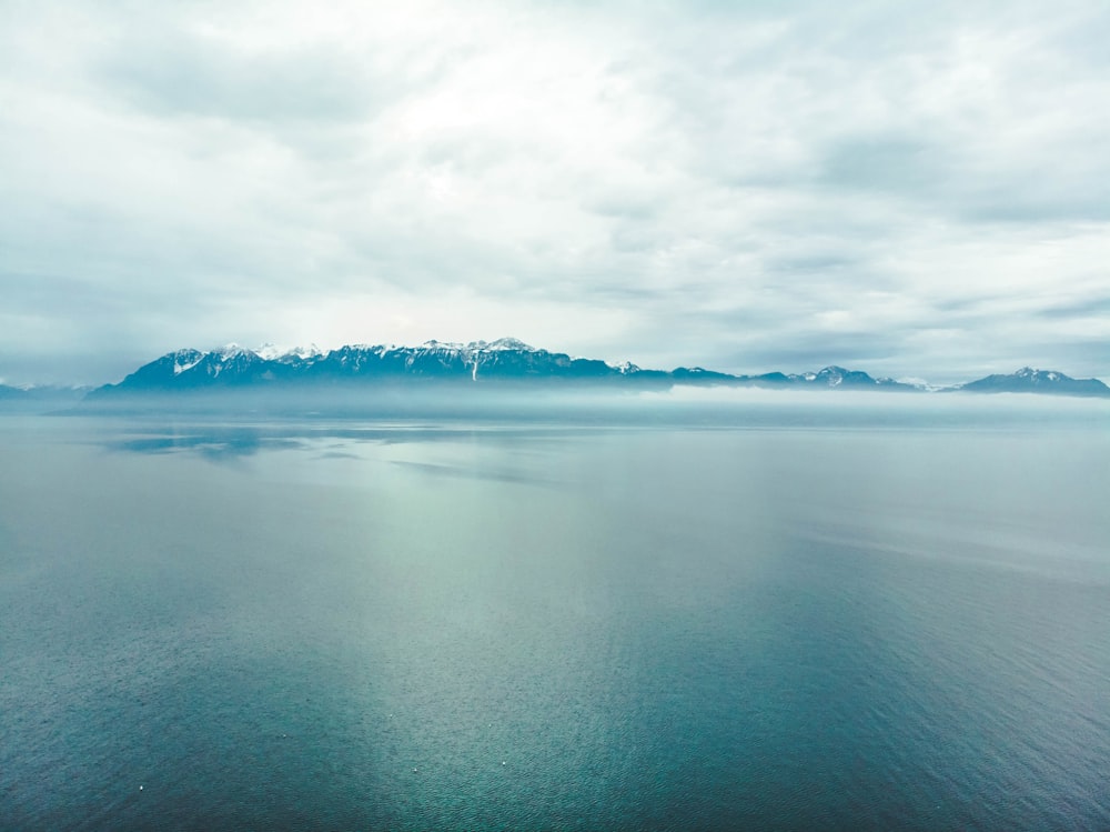 snow covered mountain beside ocean under white clouds