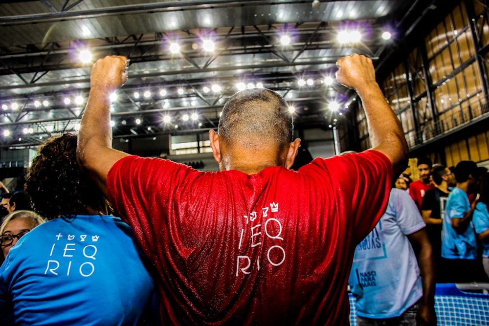 man in red shirt raising his hand inside building