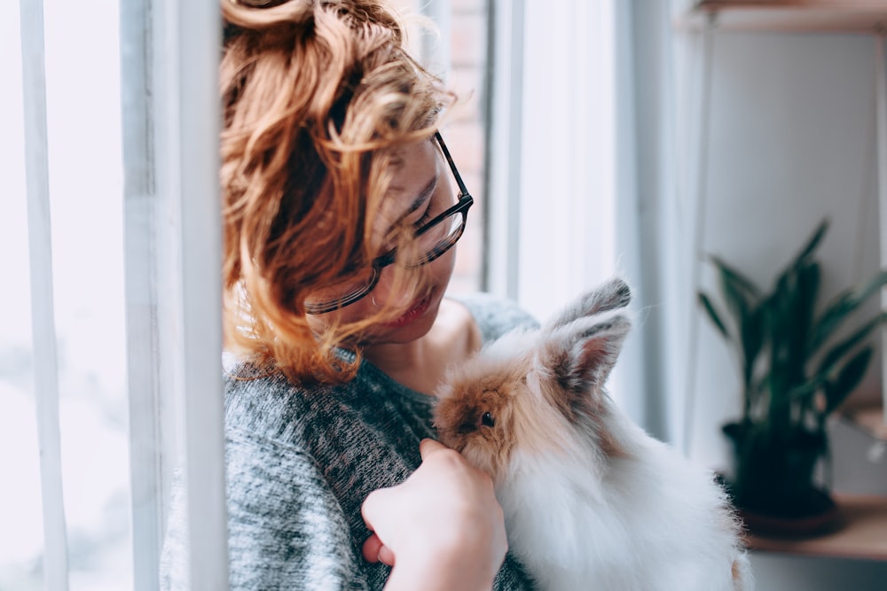 girl feeding white and brown rabbit in room