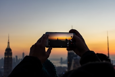 Person using a mobile phone to take a high-resolution photo of a city skyline.
