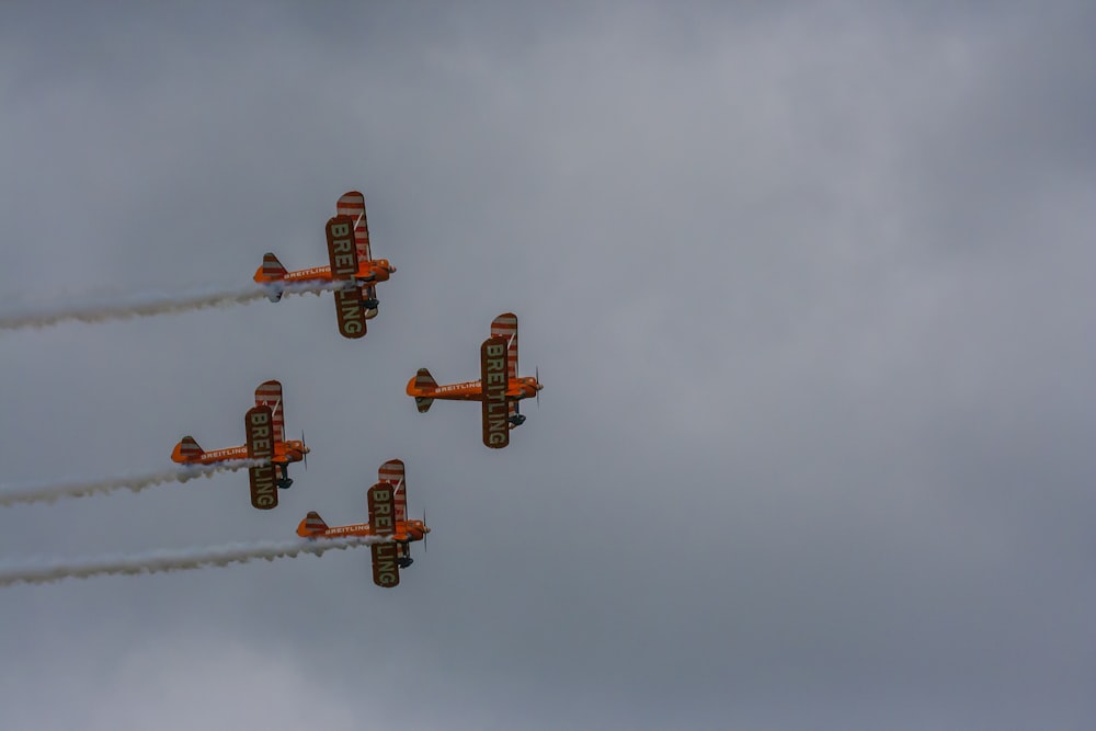four orange biplanes flying in sky