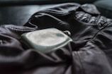 A leather jacket is laid out with a metal flask resting on top. The jacket features a prominent zipper and gathered sections at the shoulders, suggesting a sense of rugged style. The flask has a slightly worn appearance, reflecting a sense of nostalgia or adventure.