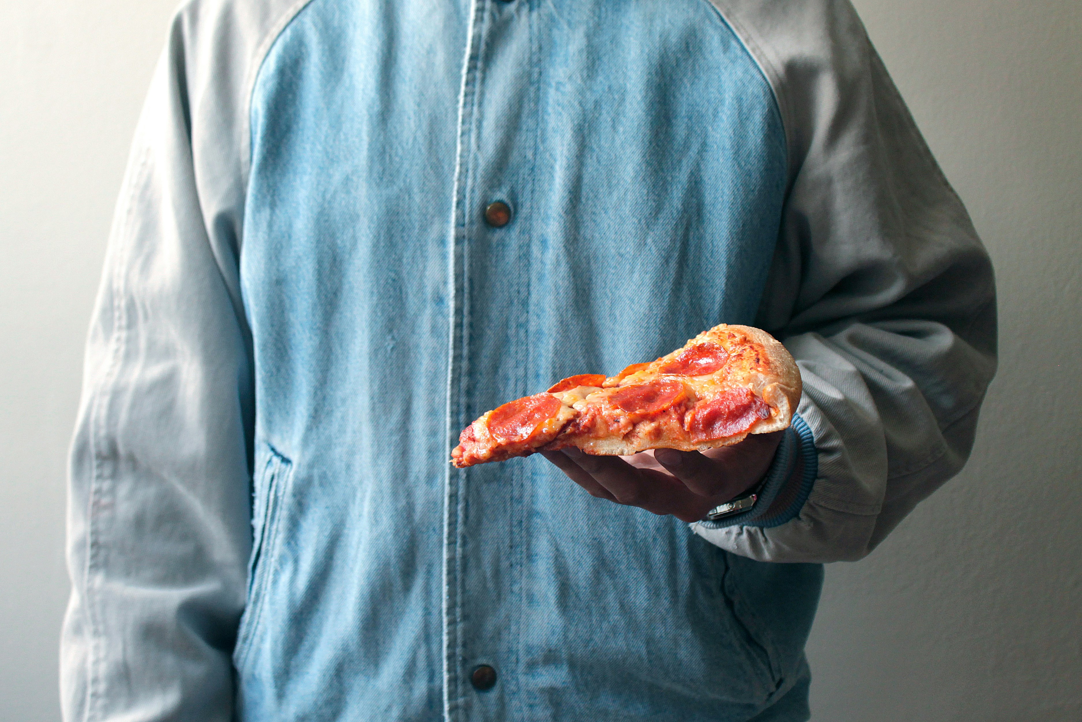 Person in denim holding a pizza slice