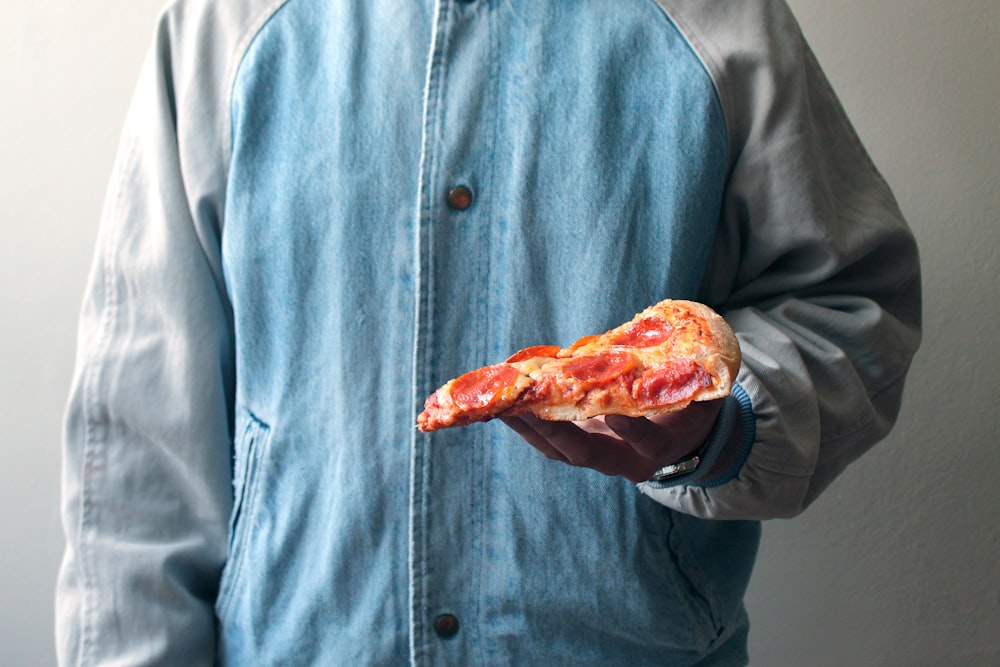 personne tenant une tranche de pizza