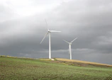 Wind turbines turning gently on a green hillside with a cloudy sky.