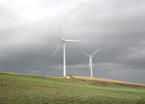 Wind turbines turning gently on a green hill with clouds above.