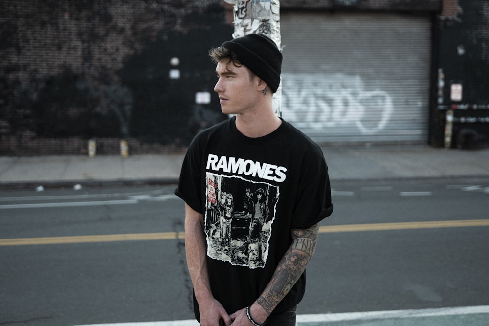 homem parado na rua vestindo camiseta preta da equipe Ramones e boné de malha preto durante o dia