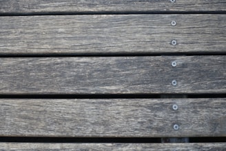 Wooden planks aligned horizontally, featuring a weathered texture with visible grain patterns. Several metal screws are evenly spaced along the center of each plank, securing them together.